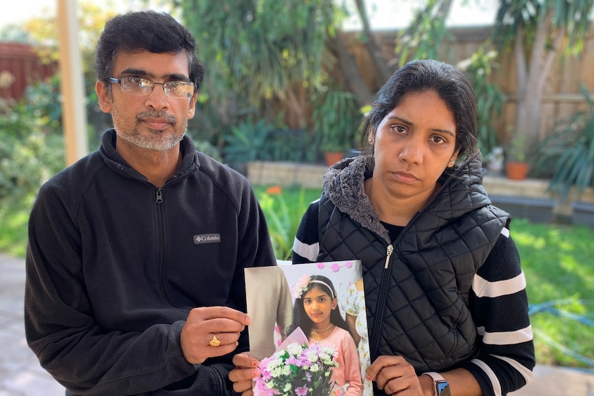 A mother and father holding a photo of their daughter