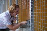 A woman crouches down to feed a treat to a dog in a cage