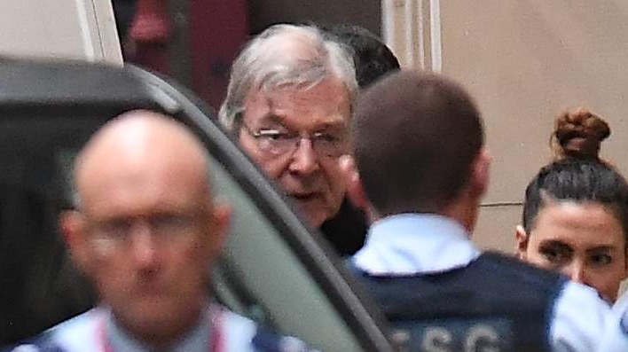 Prison guards surround George Pell as he leaves a prison van outside the stone walls of the court.