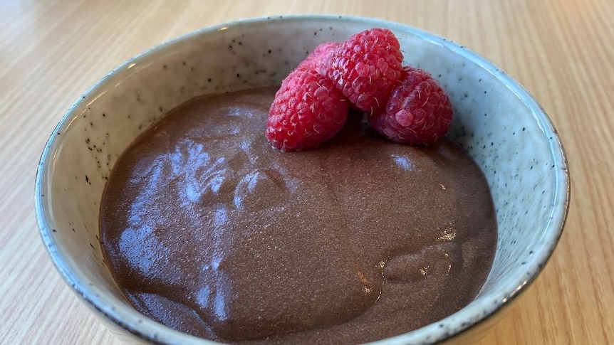 A bowl of chocolate mousse garnished with raspberries