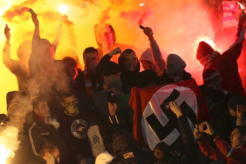 Russian football fans hold swastika flag at game.