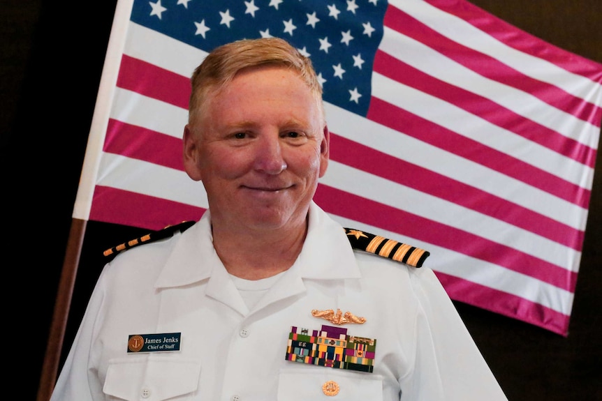 A smiling man in US navy uniform stands in front of a US flag in Exmouth, WA