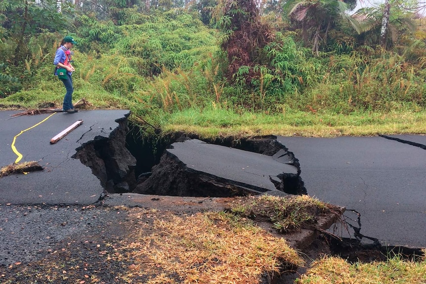 A huge crack in a road with an observer standing next to it.