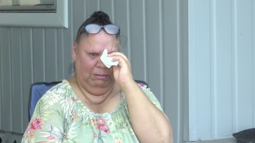 An Indigenous woman cries and wipes her eye with a tissue