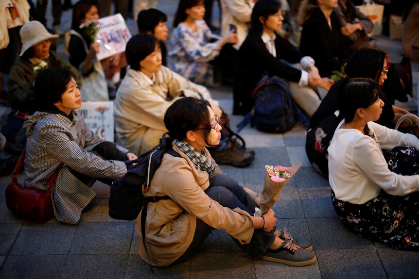 Women sit on ground holding flowers in Japan.
