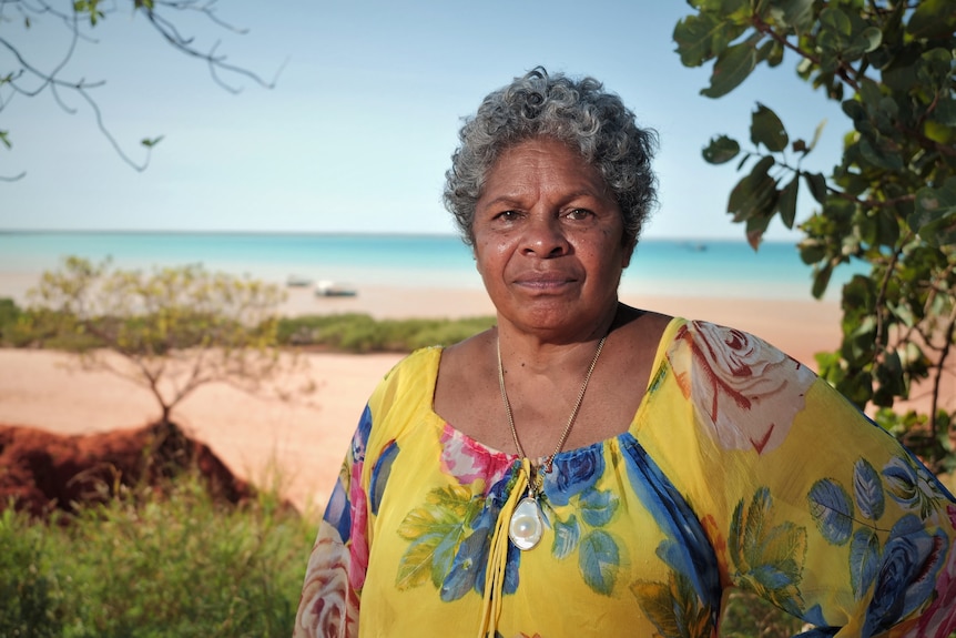 Venessa Poelina stands on the beach in Broome. She stares into the camera.