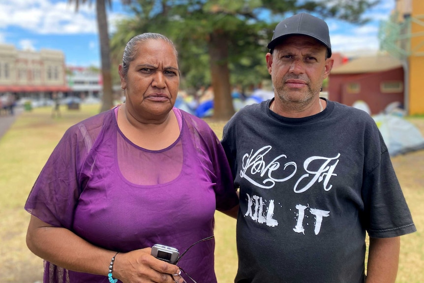 Mr Windus and Ms Culbo stand in the park, with tents behind them.