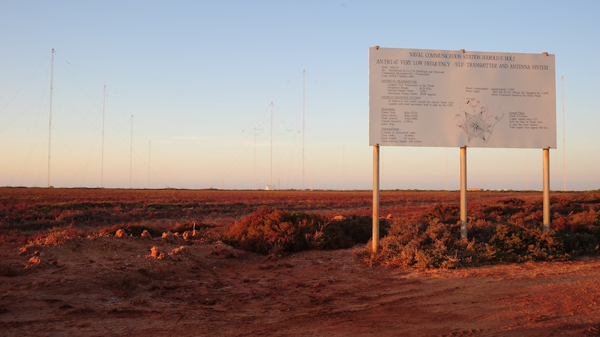 A big sign in the right handside foreground and a seires of tall antenna behind it at dusk in remote wa