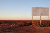 A big sign in the right handside foreground and a seires of tall antenna behind it at dusk in remote wa