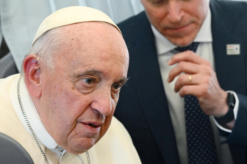The pope leans forwards as he speaks to reporters while they travel on a flight together.