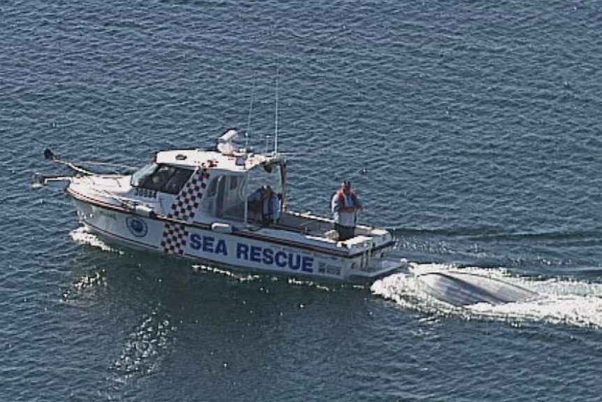 Boat tows an overturned tinny through the sea.