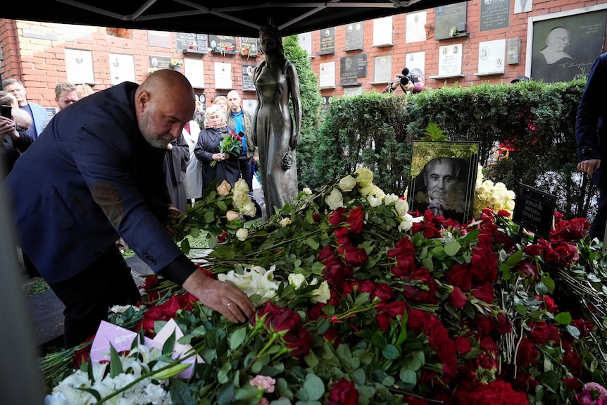 Man lays roses on the casket of former Soviet leader Mikhail Gorbachev, his portrait on top of the casket.