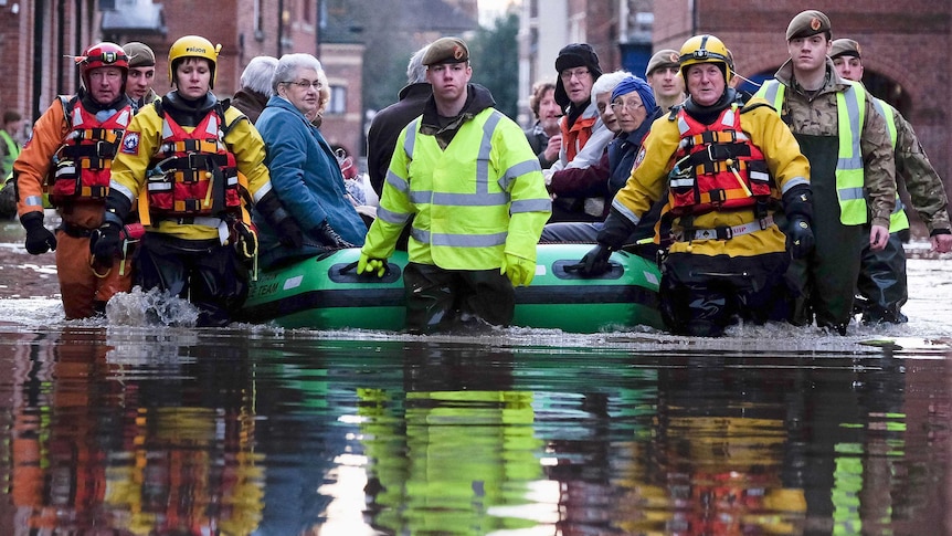 Water level view of elderly people in an inflatable boat being walked through floodwaters by soldiers and others.