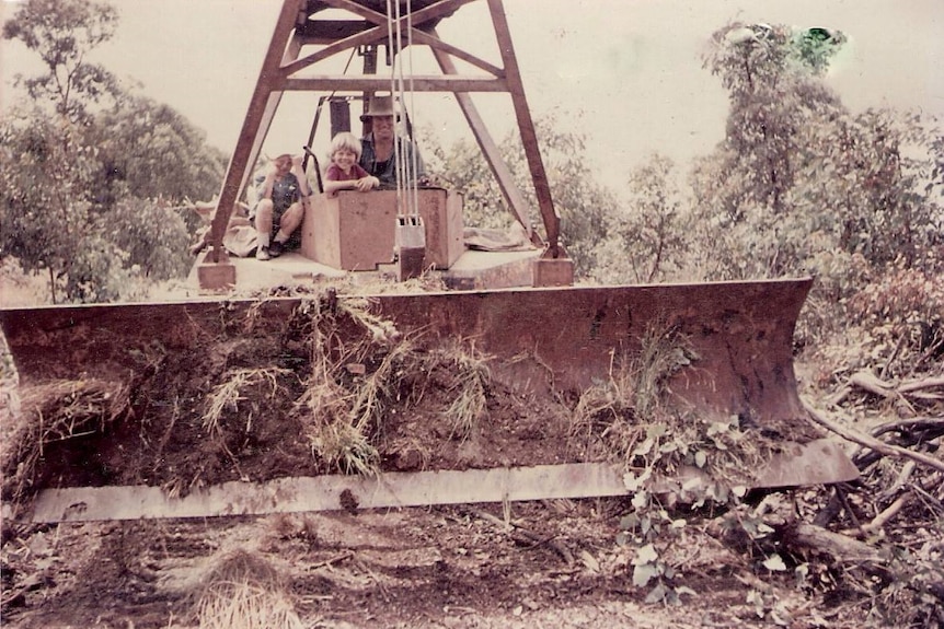 Faded colour photograph of a man on a tank with a bulldozer blade on the front, clearing land.