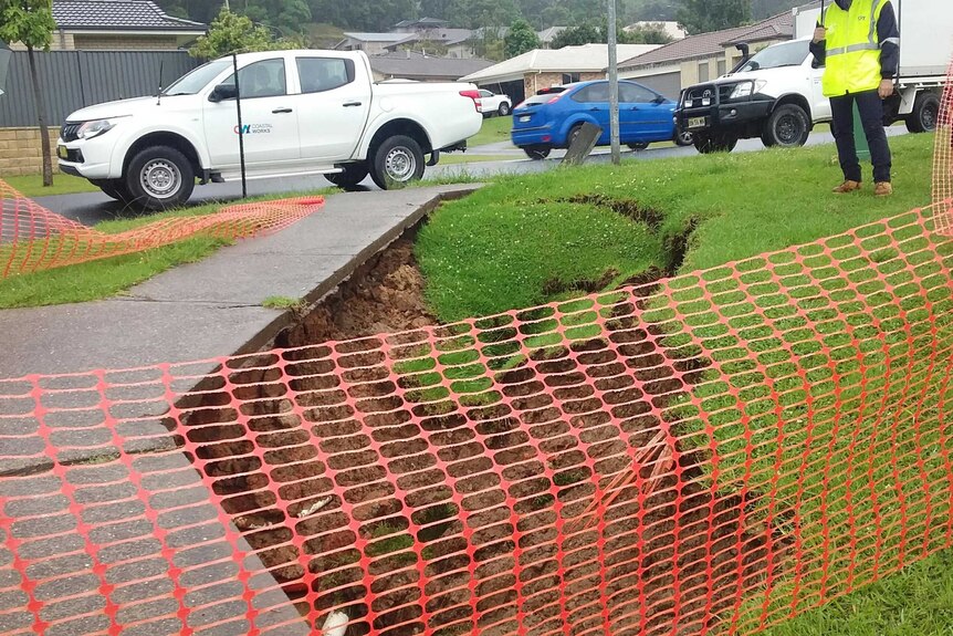An uncovered sink hole with red plastic fencing around it, green grass all around.