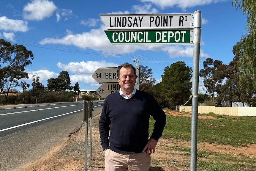 A man standing under a road sign pointing to Lindsay Point Road