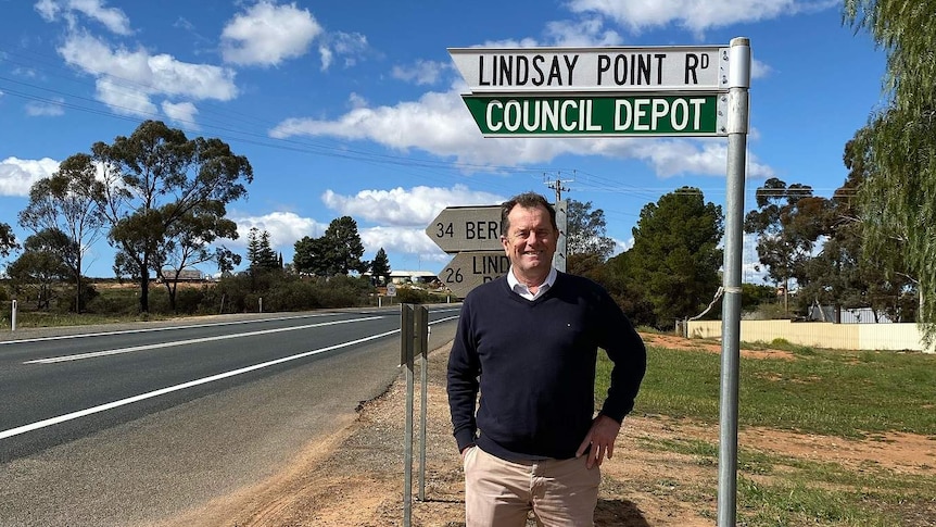 A man standing under a road sign pointing to Lindsay Point Road