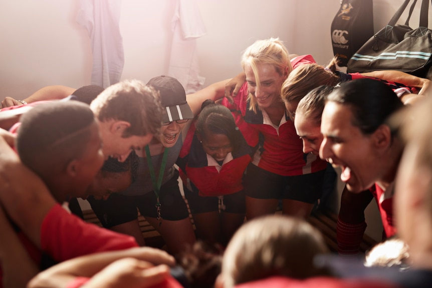 A group of community sport athletes wearing red and black gather in a circle