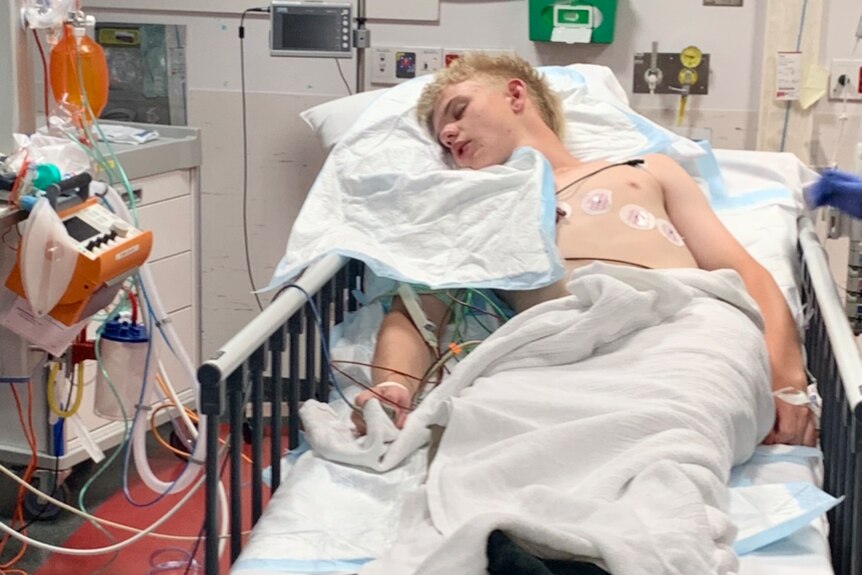 Teenage boy appears unconscious in hospital bed.