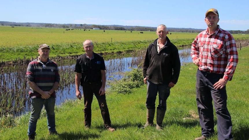 Four men stand near a river.