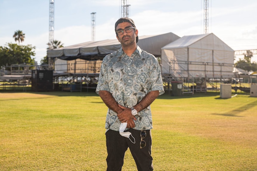 A wide shot of Saran Bajaj holding a face mask and clasping his hands in front of him.