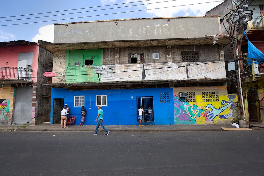 A number of men stand out the front of a blue, green and yellow building in El Chorrillo.