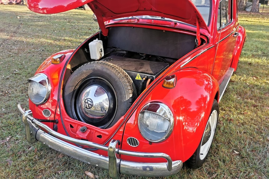 A red VW Beetle with its bonnet open showing a flat box with power cables