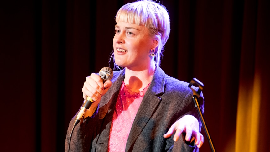 Woman in jacket talks speaks into a microphone.