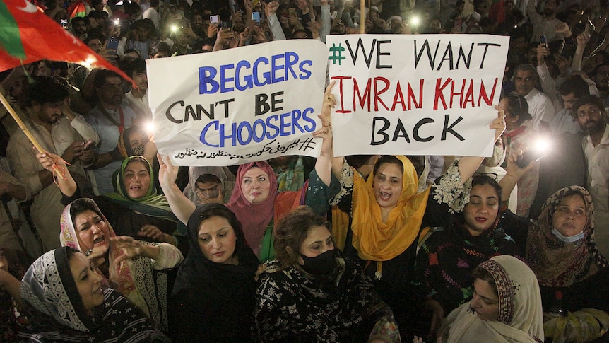 Women in a crowd hold posters reading 'Beggars can't be choosers' and 'We want Imran Khan back'