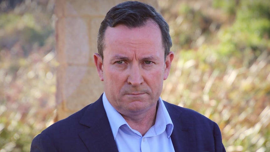 A man in a shirt and jacket addresses media at an outdoor press conference