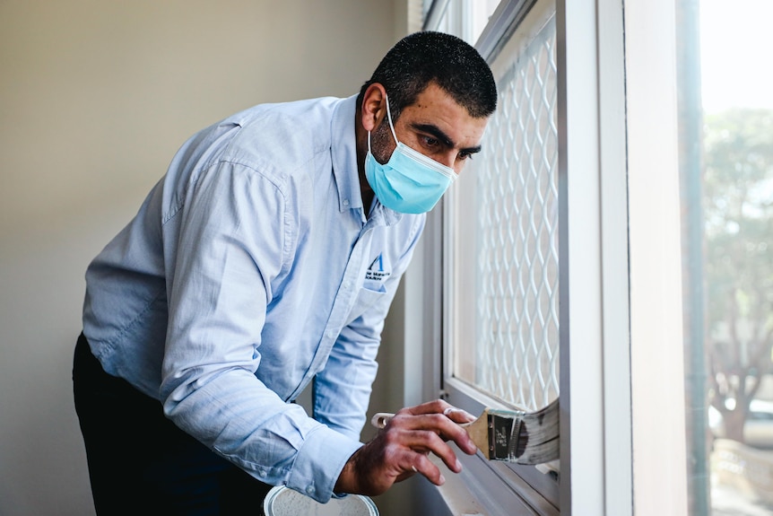 A man wearing a face mask paints a door frame.