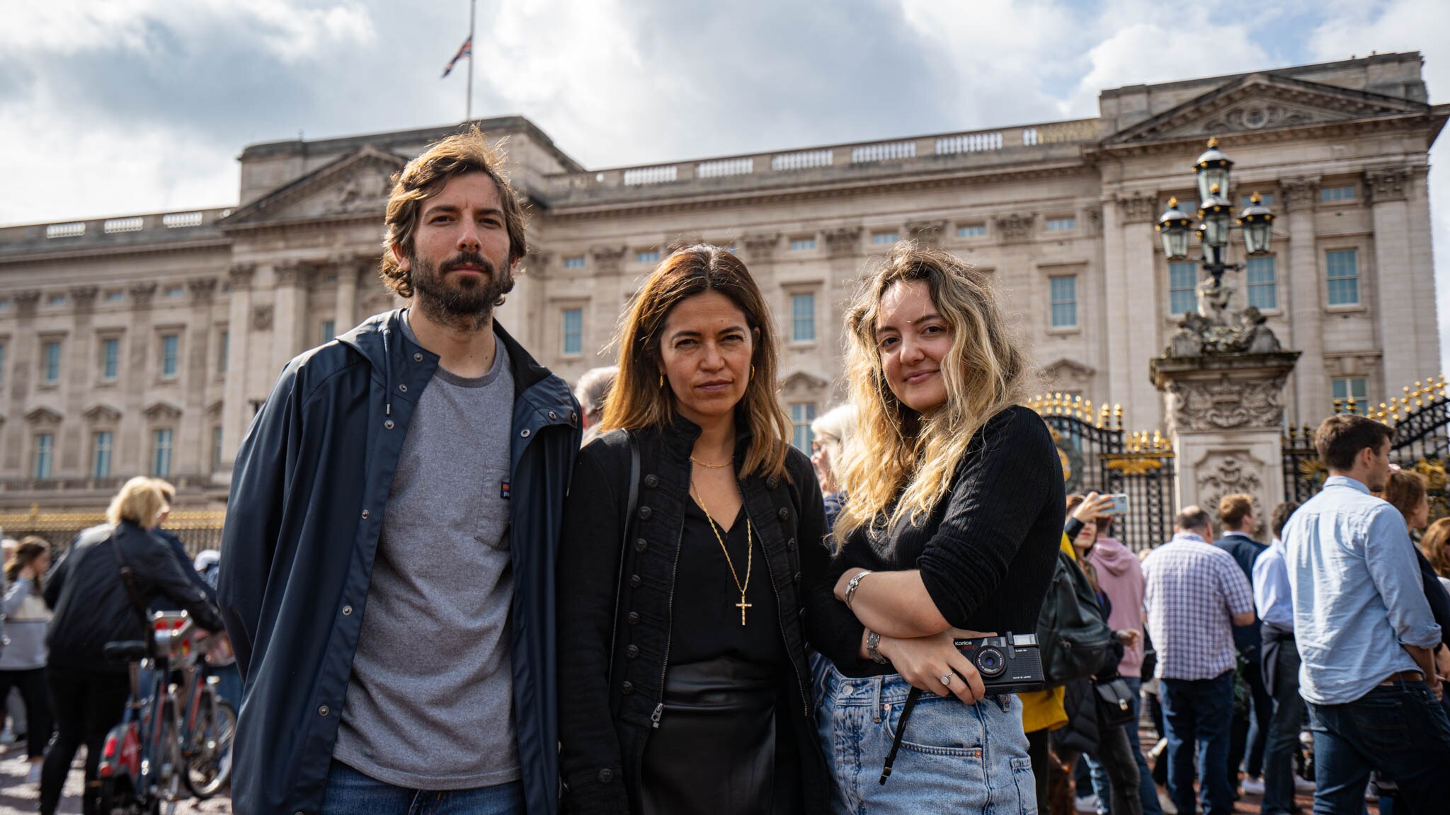 Two women and a man stand outside Buckingham Palace