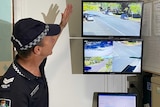 A police officer pointing to a TV screen playing security footage, inside a room.