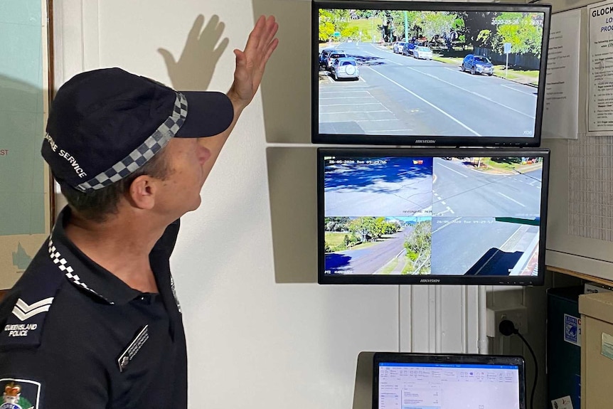 A police officer pointing to a TV screen playing security footage, inside a room.