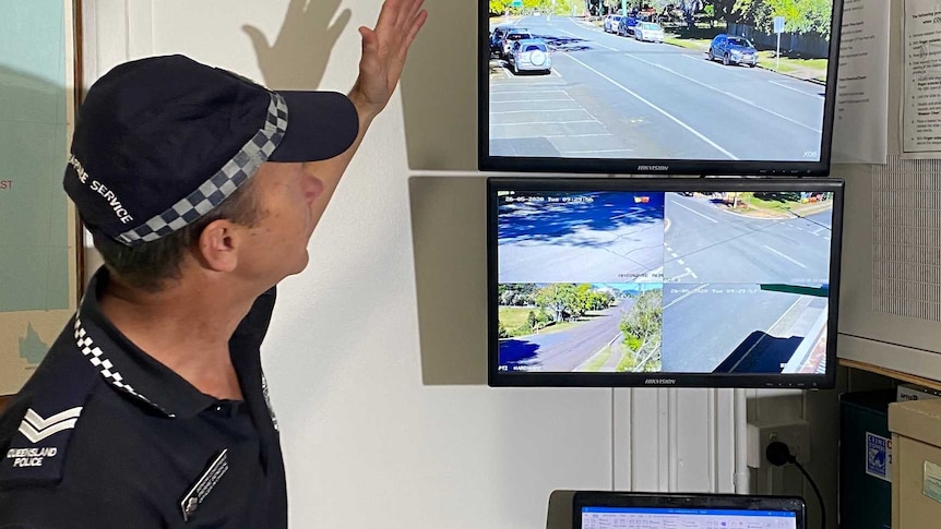 A police officer pointing to a TV screen playing security footage, inside a room.