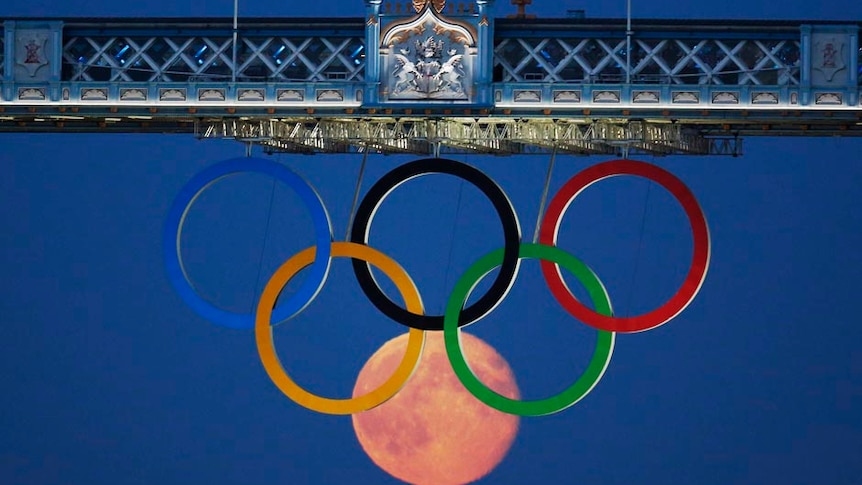 The full moon rises through the Olympic Rings hanging beneath Tower Bridge in London.