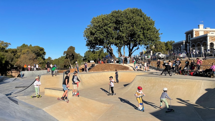 A wide shot of children riding scooters at a skate park.