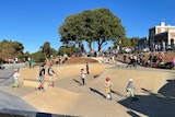 A wide shot of children riding scooters at a skate park.