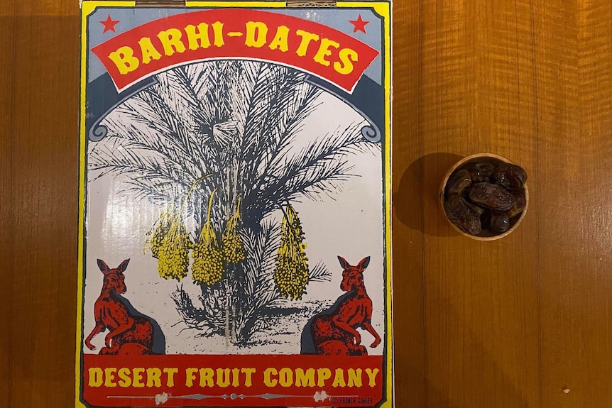 A cardboard carton of dates with "Barhi-Dates" and company name on top, with a small bowl of dates beside the box