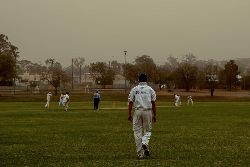 A cricket player wearing white cricket clothing is seen in the field during a red coloured dust storm in Parkes NSW.