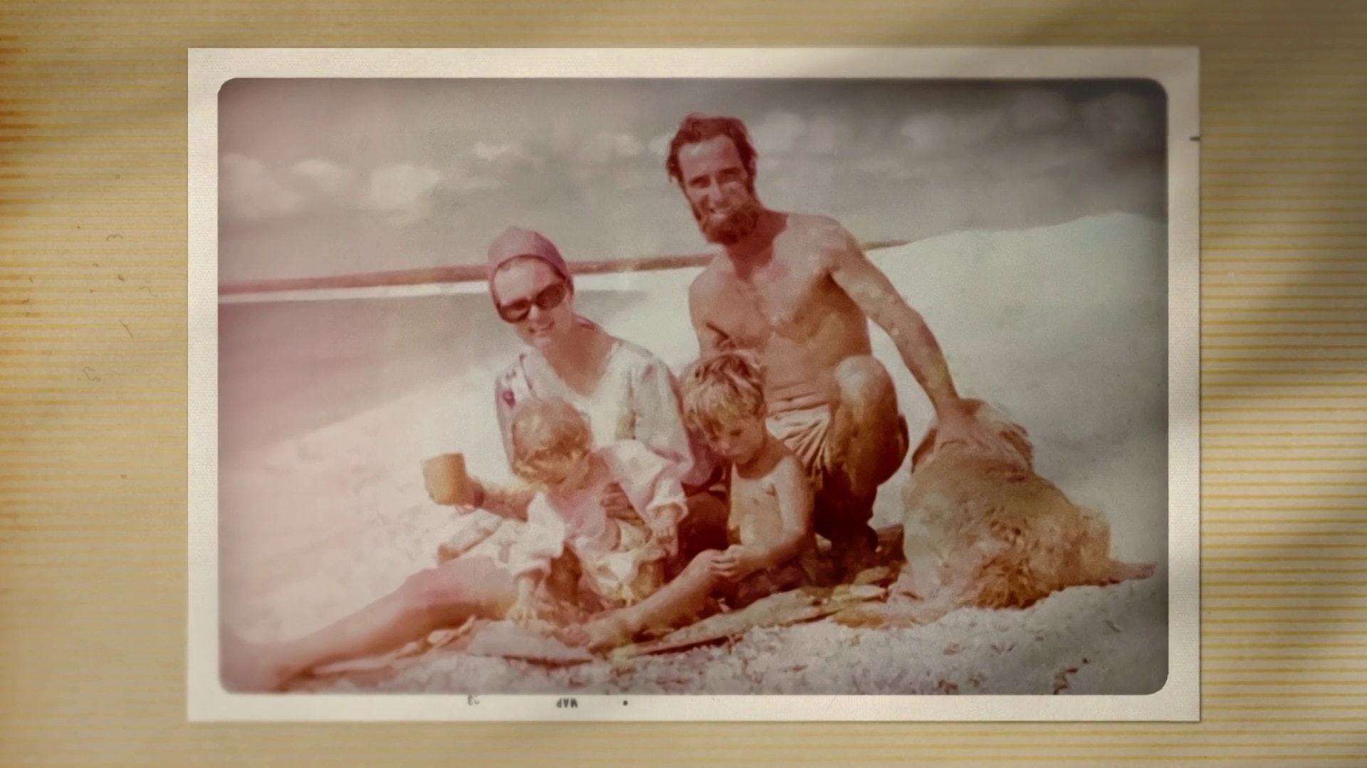 Una imagen antigua de una película de un hombre y una mujer sentados en la playa con dos niños.