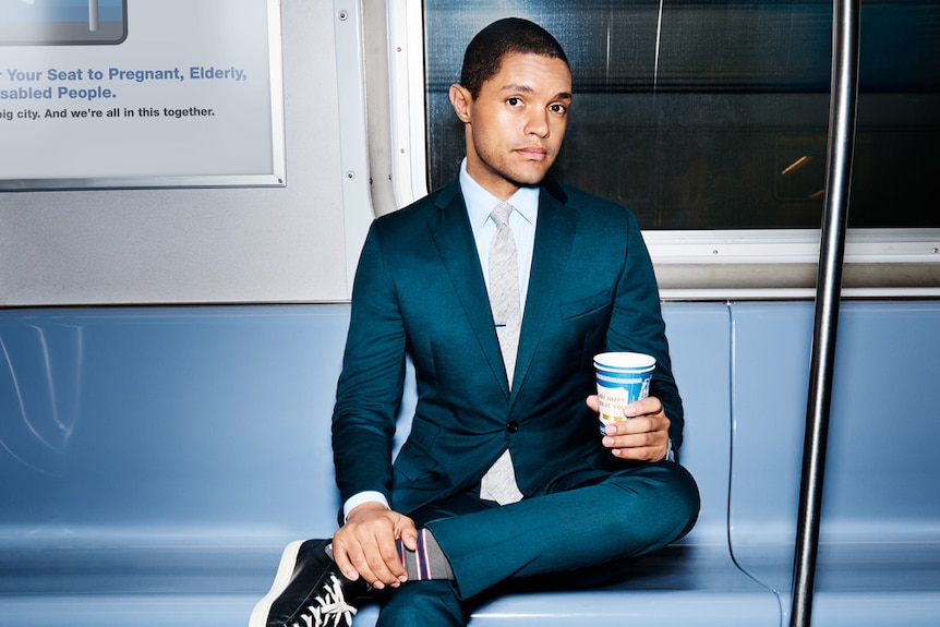 Comedian Trevor Noah holds a coffee in a subway carriage.