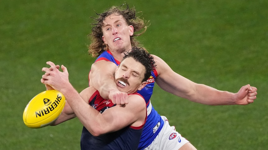 Two AFL players have a physical clash over a yellow ball on a green oval.