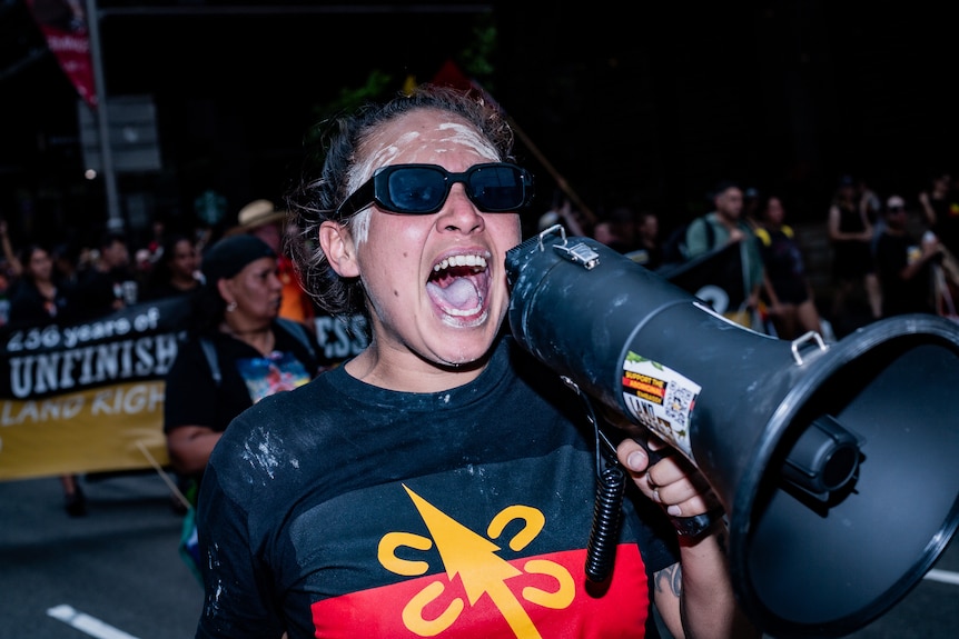 A woman yelling into a megaphone wearing glasses. 