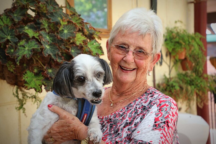 An older woman with short white hair and a red and grey top holding her dog
