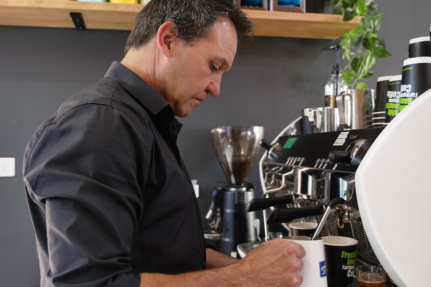 A man standing behind a cafe coffee machine making coffee.
