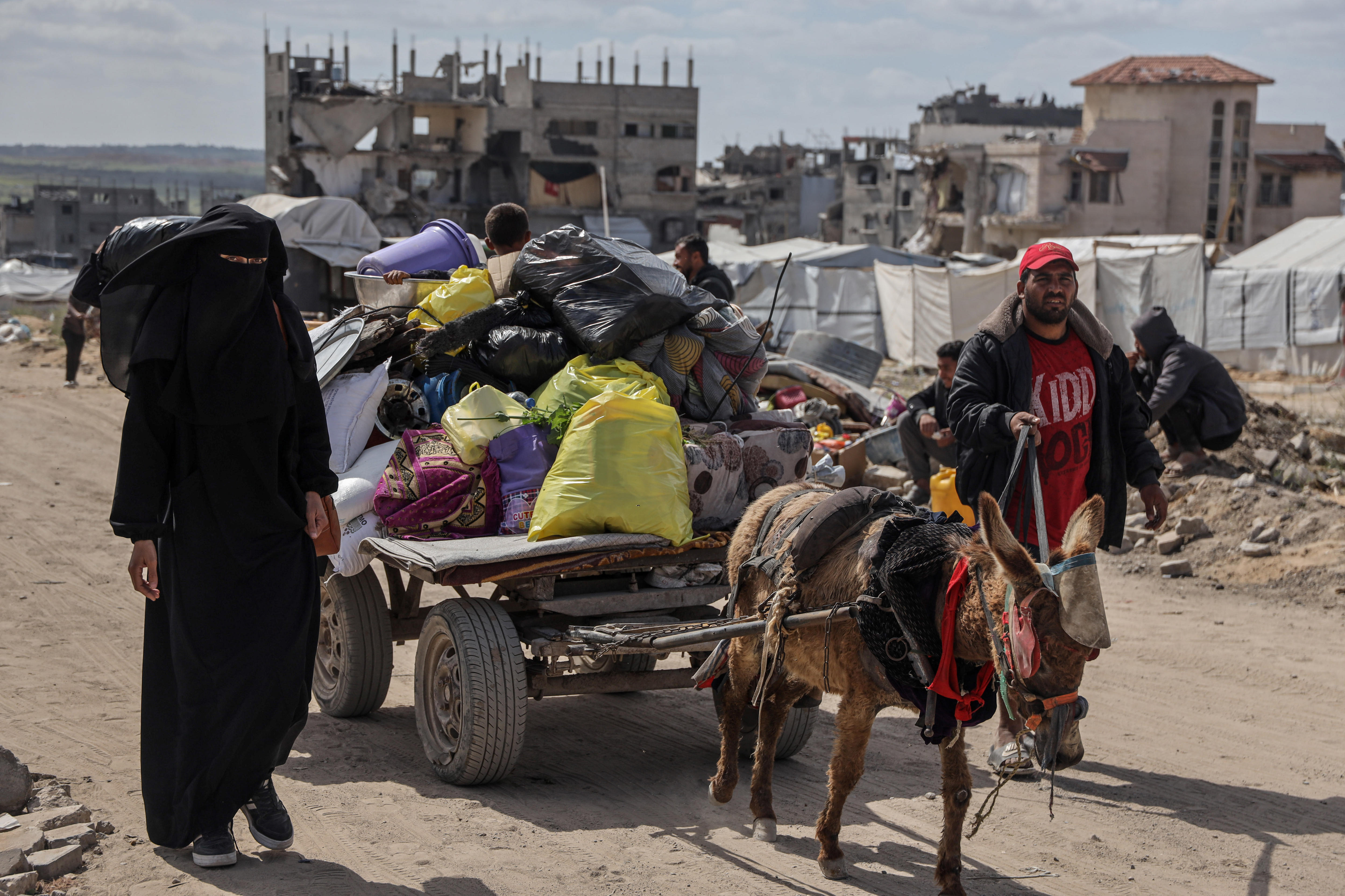 A Palestinian family walking with a donkey-drawn cart full of items and plastic bags. 