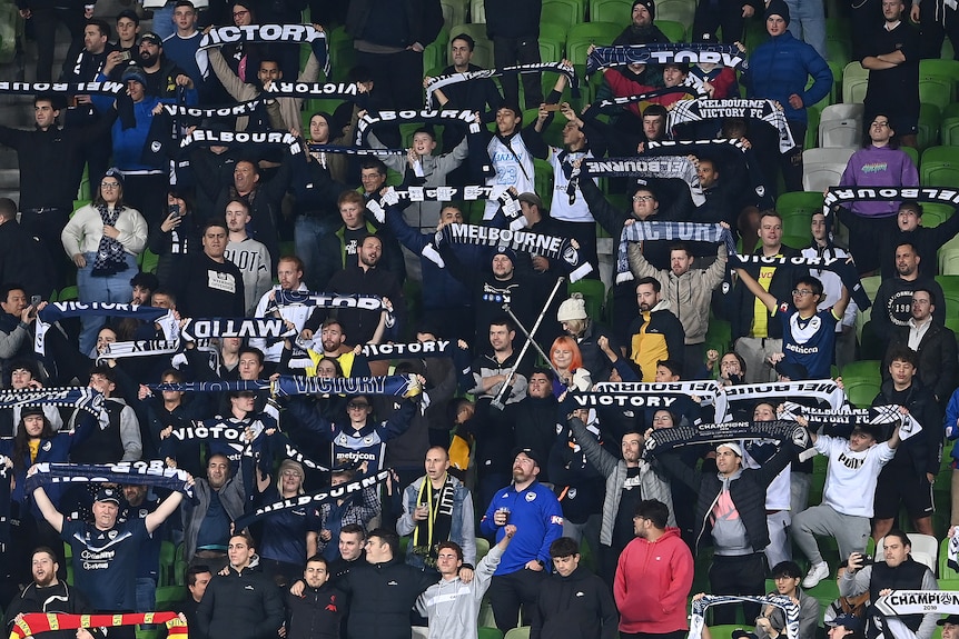 Melbourne Victory fans stand and hold scarves above their heads