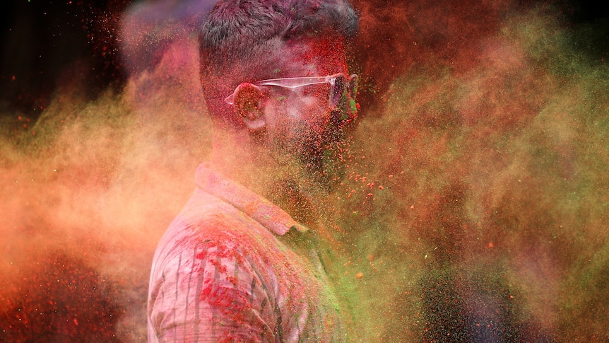 A bearded man with sunglasses is pictured as brightly coloured powders are flying in the air around him.