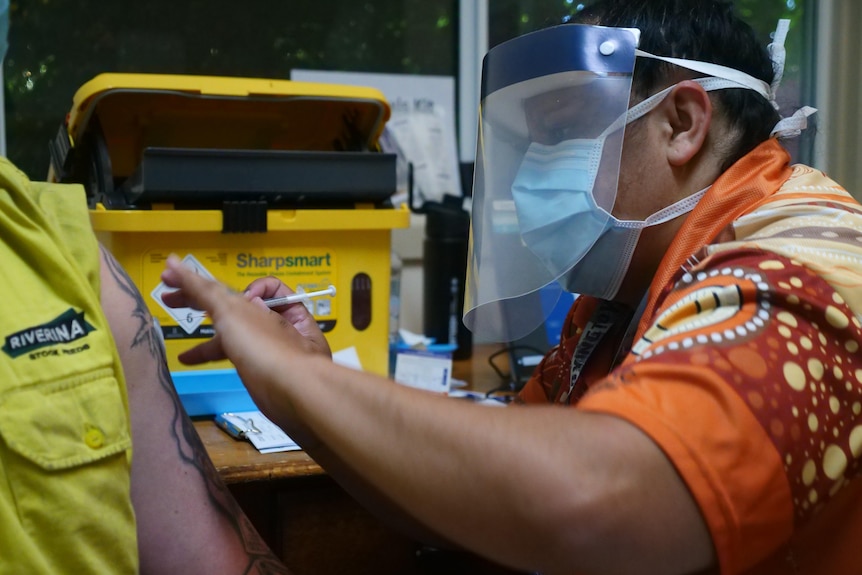 A person in a mask and face shield gives another person a vaccination.